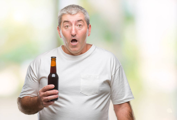 Beau vieillard buvant une bouteille de bière sur fond isolé effrayé en état de choc avec un visage surprise, effrayé et excité par l'expression de la peur
 - Photo, image