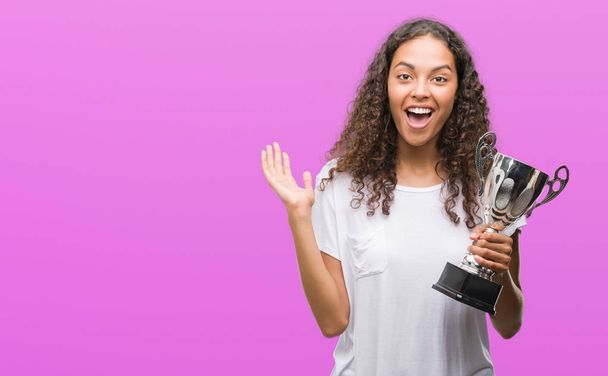 Mladá žena hispánský drží trofej vítěze velmi šťastný a nadšený, výraz slaví vítězství křičet s velkým úsměvem a pozvedl ruce - Fotografie, Obrázek