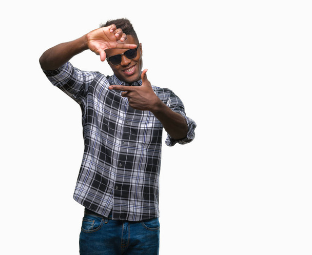 Young african american man wearing sunglasses over isolated background smiling making frame with hands and fingers with happy face. Creativity and photography concept. - Photo, Image