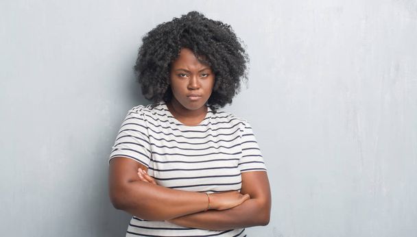 Young african american plus size woman over grey grunge wall skeptic and nervous, disapproving expression on face with crossed arms. Negative person. - Photo, Image