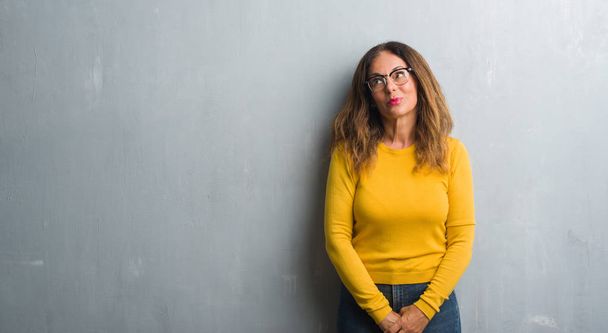 Middle age hispanic woman over grey wall wearing glasses smiling looking side and staring away thinking. - Zdjęcie, obraz