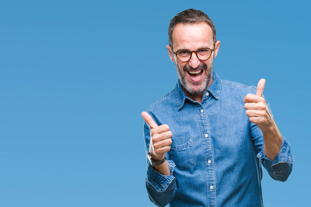 Middle age hoary senior man wearing glasses over isolated background success sign doing positive gesture with hand, thumbs up smiling and happy. Looking at the camera with cheerful expression, winner gesture. - Photo, Image