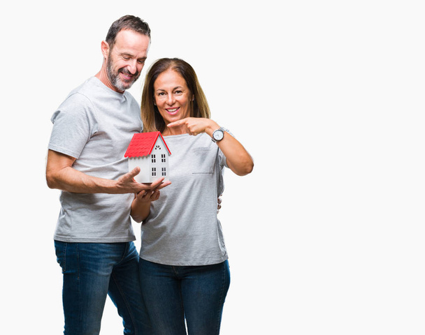 Middle age hispanic casual couple buying new house over isolated background very happy pointing with hand and finger - Foto, afbeelding