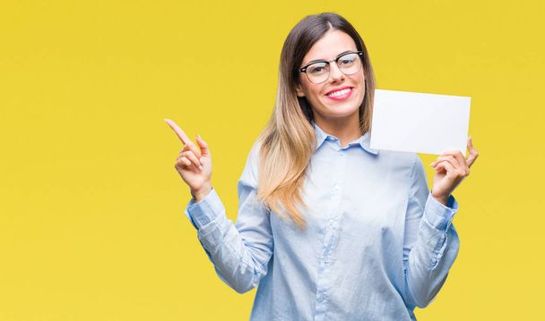 Jovem mulher de negócios bonita segurando cartão em branco sobre fundo isolado muito feliz apontando com a mão e o dedo para o lado
 - Foto, Imagem