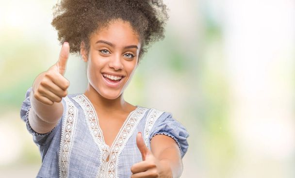 手で、肯定的なジェスチャーをして承認する孤立した背景に若いアフロ ・ アメリカ人女性は親指笑顔と幸せな成功のためです。カメラ、勝者のジェスチャーを見てください。. - 写真・画像