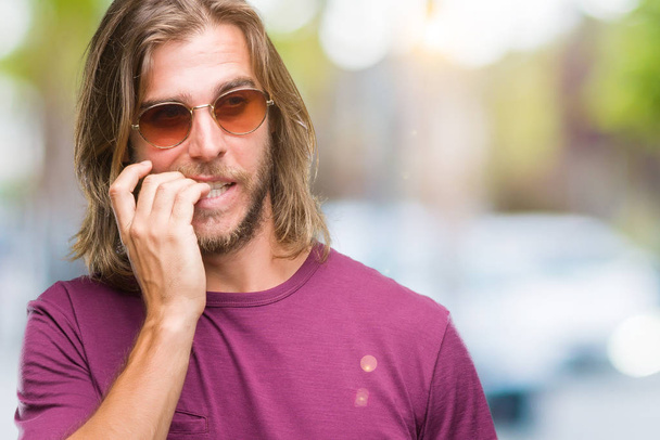 Young handsome man with long hair wearing sunglasses over isolated background looking stressed and nervous with hands on mouth biting nails. Anxiety problem. - Fotó, kép
