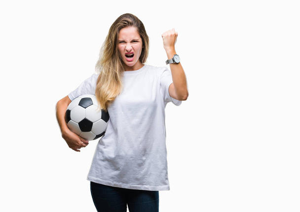 Молодая красивая блондинка держит футбольный мяч на изолированном фоне раздраженный и разочарованный кричать от гнева, сумасшедший и кричать с поднятой рукой, гнев концепции
 - Фото, изображение