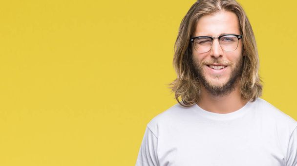 Mladý pohledný muž s dlouhými vlasy, nosí brýle izolované pozadí mrkání, při pohledu na fotoaparát se sexy výraz, veselý a šťastný obličej. - Fotografie, Obrázek