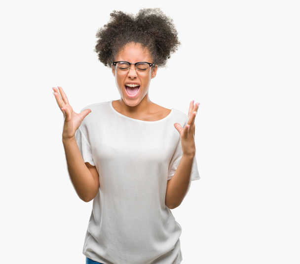 Giovane donna afro-americana con gli occhiali su sfondo isolato che celebra pazzo e pazzo per il successo con le braccia alzate e gli occhi chiusi urlando eccitato. Concetto vincitore
 - Foto, immagini
