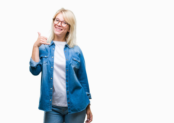 Jonge mooie blonde vrouw bril over geïsoleerde achtergrond doen glimlachen telefoon gebaar met hand en vingers als praten aan de telefoon. Concepten communiceren. - Foto, afbeelding
