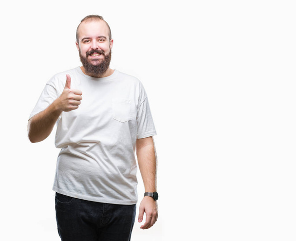 Joven hombre hipster caucásico que usa una camiseta casual sobre un fondo aislado haciendo un gesto feliz de pulgares hacia arriba con la mano. Aprobar la expresión mirando a la cámara con éxito
. - Foto, imagen