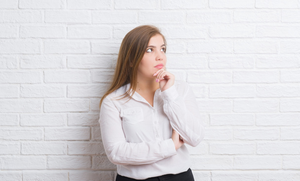 Young adult business woman over white brick wall serious face thinking about question, very confused idea - Foto, imagen