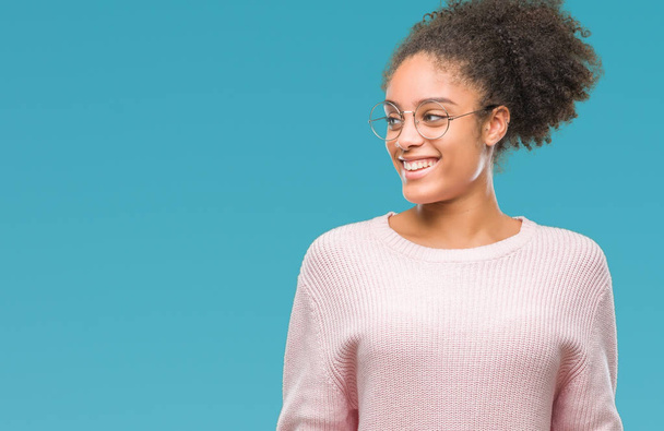 Молодая афро-американка в очках на изолированном фоне смотрит в сторону с улыбкой на лице, естественным выражением лица. Смеясь уверенно
. - Фото, изображение