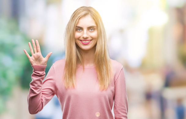 Nuori kaunis blondi nainen yllään vaaleanpunainen talvi villapaita yli eristetty tausta näyttää ja osoittaa sormilla numero viisi hymyillen itsevarma ja onnellinen
. - Valokuva, kuva