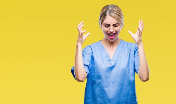 Young beautiful blonde doctor surgeon nurse woman over isolated background celebrating mad and crazy for success with arms raised and closed eyes screaming excited. Winner concept - Photo, Image