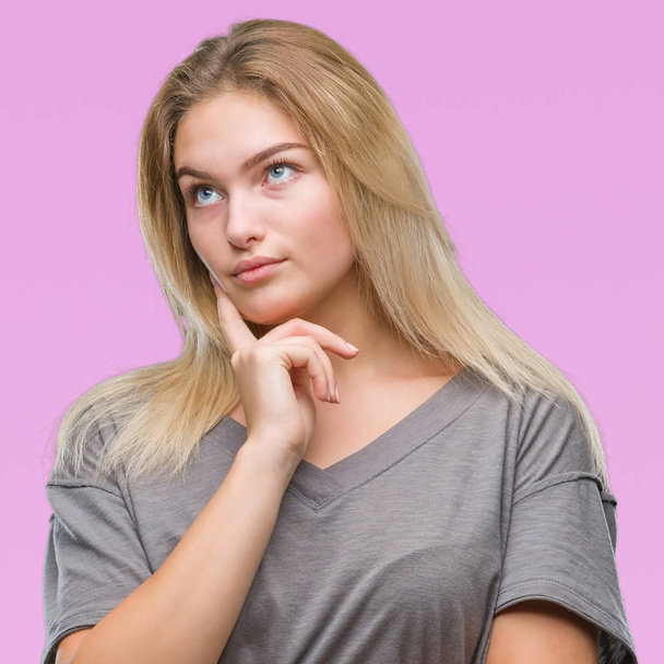 Young caucasian woman over isolated background with hand on chin thinking about question, pensive expression. Smiling with thoughtful face. Doubt concept. - Foto, afbeelding