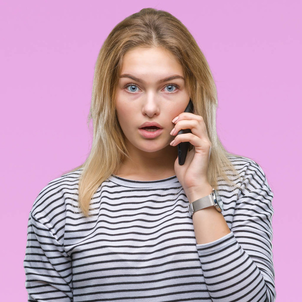 Young caucasian woman showing smartphone screen over isolated background scared in shock with a surprise face, afraid and excited with fear expression - Фото, изображение