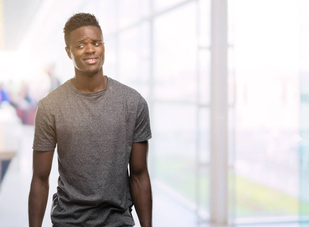 Giovane uomo afro-americano con indosso t-shirt grigia sorridente guardando lato e fissando via pensando
. - Foto, immagini