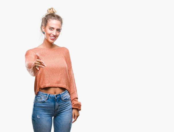 Beautiful young blonde woman over isolated background smiling friendly offering handshake as greeting and welcoming. Successful business. - Foto, Imagem