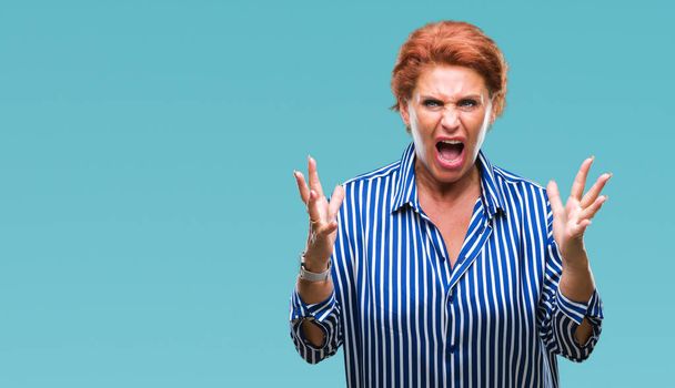 Atrractive senior caucasian redhead woman over isolated background crazy and mad shouting and yelling with aggressive expression and arms raised. Frustration concept. - Photo, Image