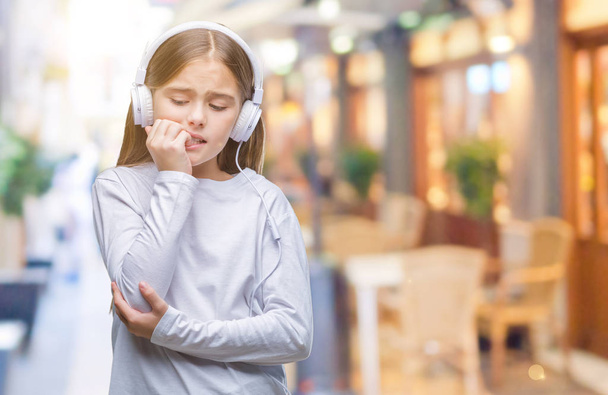 Mooi meisje dragen koptelefoon luisteren naar muziek op geïsoleerde achtergrond op zoek gestresst en nerveus met handen op mond nagels te bijten. Angst probleem. - Foto, afbeelding