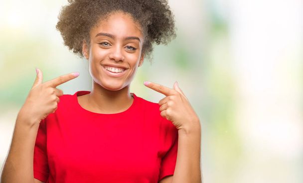 Young afro american woman over isolated background smiling confident showing and pointing with fingers teeth and mouth. Health concept. - Photo, Image