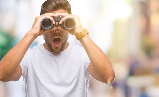 Young handsome man looking through binoculars over isolated background scared in shock with a surprise face, afraid and excited with fear expression - Photo, Image
