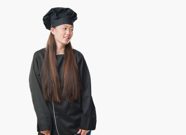 Молода Китайська жінка над ізольовані фон носіння шеф-кухар рівномірного фотографіях хтось дивитися вбік сторону з усмішкою на обличчі, натуральному вираженні. Сміючись впевнено. - Фото, зображення