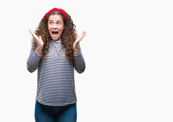 Beautiful brunette curly hair young girl wearing stripes sweater over isolated background celebrating surprised and amazed for success with arms raised and open eyes. Winner concept. - Photo, Image
