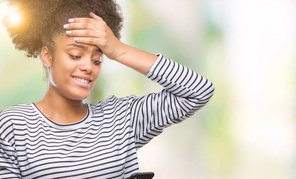 junge Afroamerikanerin, die mit dem Smartphone über isolierten Hintergrund SMS schreibt, gestresst mit der Hand auf dem Kopf, schockiert vor Scham und Überraschung, wütend und frustriert. Angst und Verärgerung wegen Fehlern. - Foto, Bild