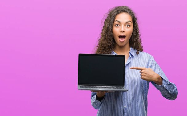 Молода іспаномовна жінка тримає комп'ютерний ноутбук дуже щасливий вказуючи рукою і пальцем
 - Фото, зображення