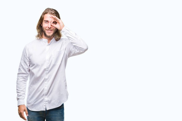 Young handsome man with long hair over isolated background doing ok gesture with hand smiling, eye looking through fingers with happy face. - Photo, image