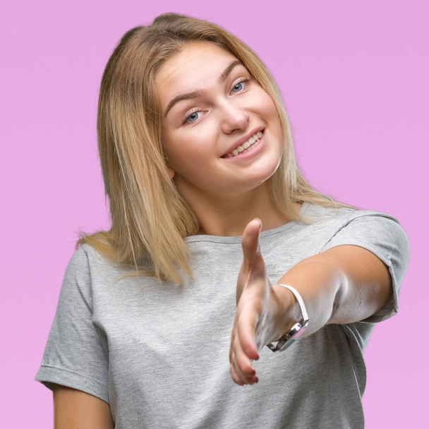 Young caucasian woman over isolated background smiling friendly offering handshake as greeting and welcoming. Successful business. - Фото, зображення