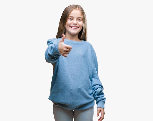 Young beautiful girl wearing winter sweater over isolated background doing happy thumbs up gesture with hand. Approving expression looking at the camera with showing success. - Фото, зображення