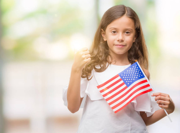 Brunette hispanic girl holding flag of United States of America happy with big smile doing ok sign, thumb up with fingers, excellent sign - 写真・画像