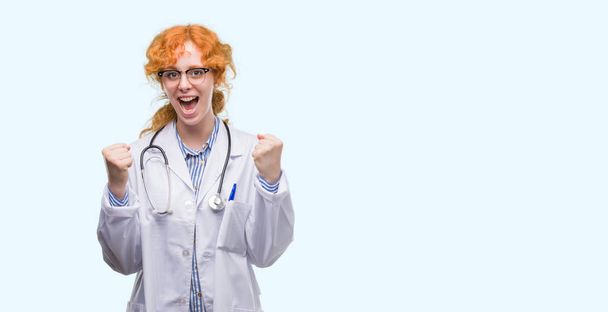 若い赤毛の女性医師制服を祝っている身に着けている驚いて腕を上げると成功のため驚くし、目を開きます。勝者の概念. - 写真・画像