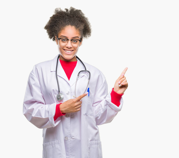 Jonge afro Amerikaanse dokter vrouw over geïsoleerde achtergrond glimlachen en kijken naar de camera met twee handen en vingers wijzen naar de kant. - Foto, afbeelding