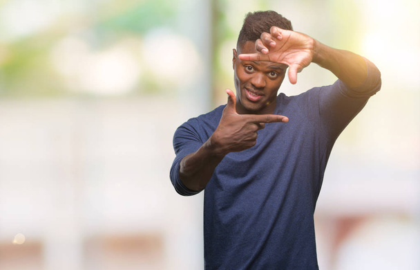 Молодой африканский американец на изолированном фоне улыбается делая рамку с руками и пальцами со счастливым лицом. Концепция творчества и фотографии
. - Фото, изображение