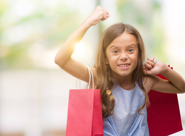 Brunette hispanic girl holding shopping bags annoyed and frustrated shouting with anger, crazy and yelling with raised hand, anger concept - Foto, Imagen
