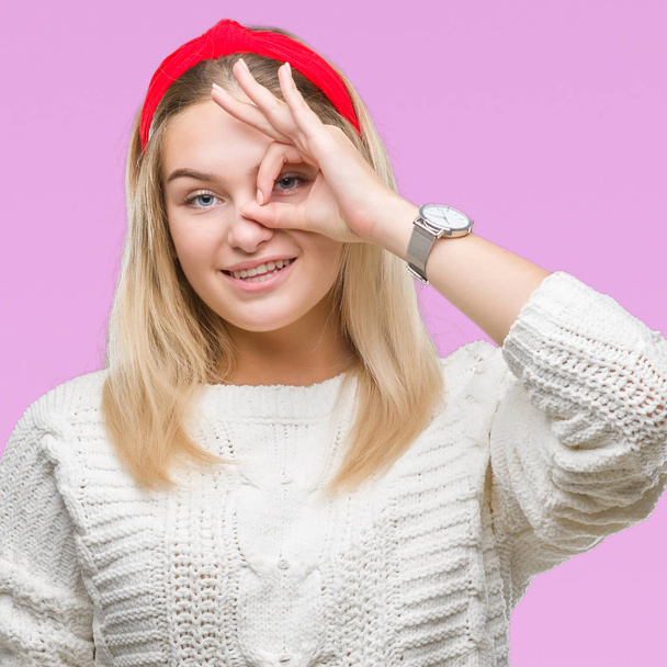Jeune femme caucasienne portant un pull d'hiver sur fond isolé faisant un geste correct avec la main souriante, les yeux regardant à travers les doigts avec un visage heureux
. - Photo, image