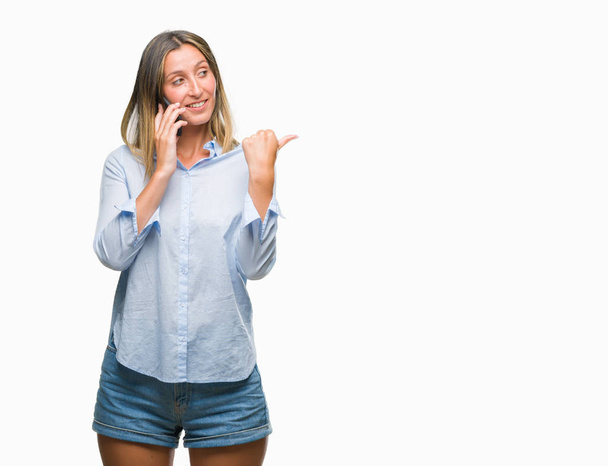 Young beautiful woman talking on smartphone over isolated background pointing and showing with thumb up to the side with happy face smiling - Photo, Image