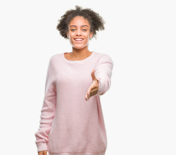 Joven mujer afroamericana vistiendo suéter de invierno sobre fondo aislado sonriendo amigable ofreciendo apretón de manos como saludo y bienvenida. Negocios exitosos
. - Foto, Imagen