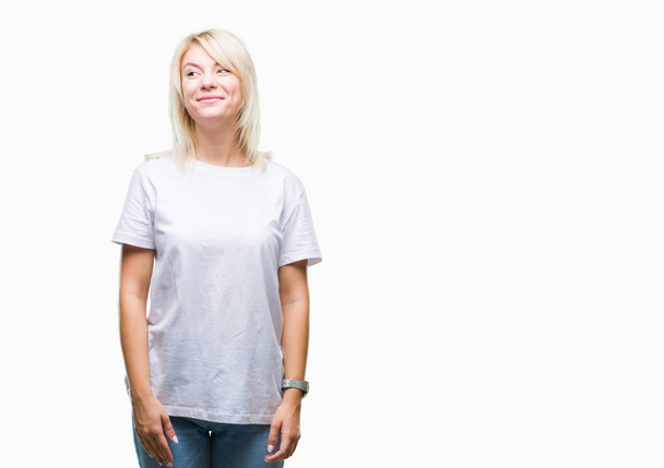 junge schöne blonde Frau trägt weißes T-Shirt über isoliertem Hintergrund, lächelt Seite und starrt denken weg. - Foto, Bild