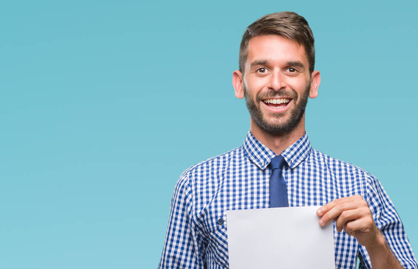 Young handsome man holding blank paper over isolated background with a happy face standing and smiling with a confident smile showing teeth - Photo, Image