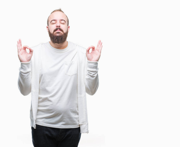 Young caucasian hipster man wearing sport clothes over isolated background relax and smiling with eyes closed doing meditation gesture with fingers. Yoga concept. - Фото, зображення