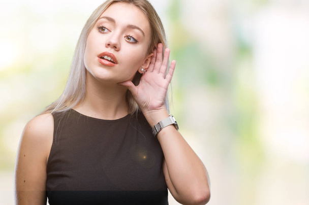 Jeune femme blonde sur fond isolé souriant main contre oreille en écoutant une rumeur ou des commérages. Concept de surdité
. - Photo, image
