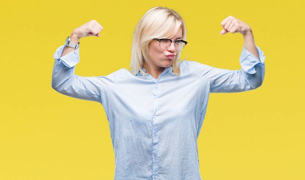 Young beautiful blonde business woman wearing glasses over isolated background showing arms muscles smiling proud. Fitness concept. - Photo, Image