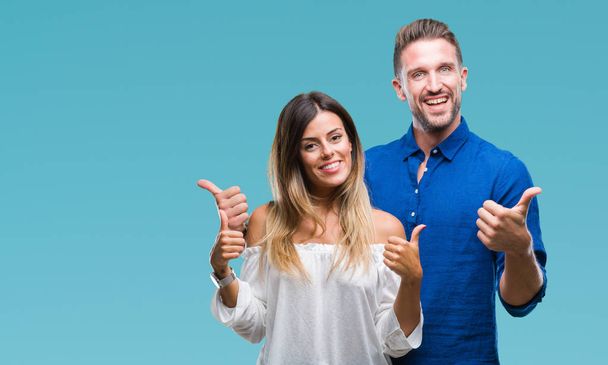 Young couple in love over isolated background success sign doing positive gesture with hand, thumbs up smiling and happy. Looking at the camera with cheerful expression, winner gesture. - Photo, Image