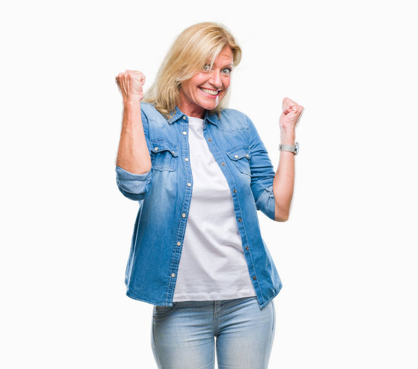 Middle age blonde woman over isolated background very happy and excited doing winner gesture with arms raised, smiling and screaming for success. Celebration concept. - Фото, зображення