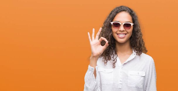 Jeune femme hispanique portant des lunettes de soleil faisant signe ok avec les doigts, excellent symbole
 - Photo, image
